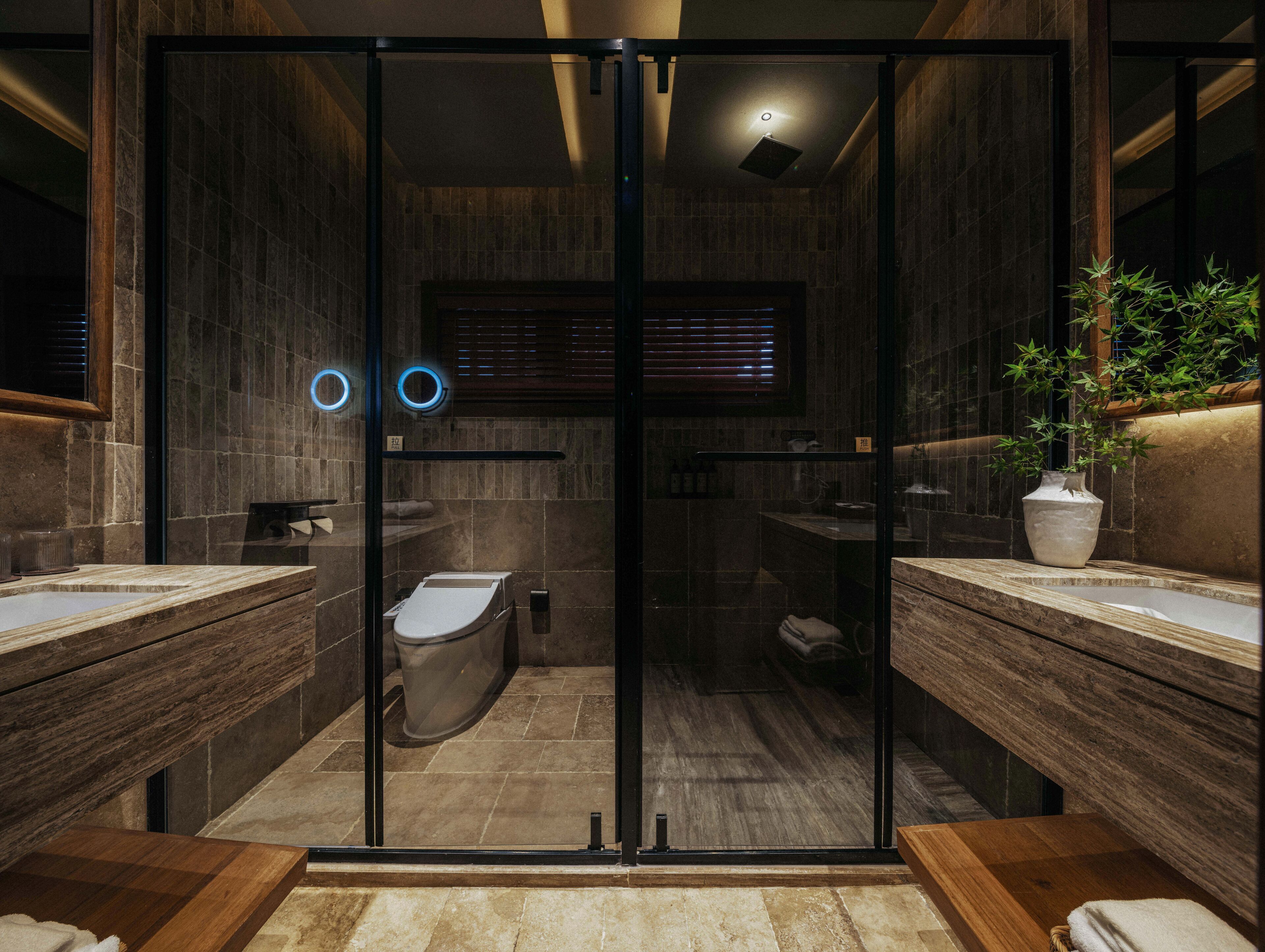 A modern bathroom with a glass partition, two sinks, a toilet, and a shower.