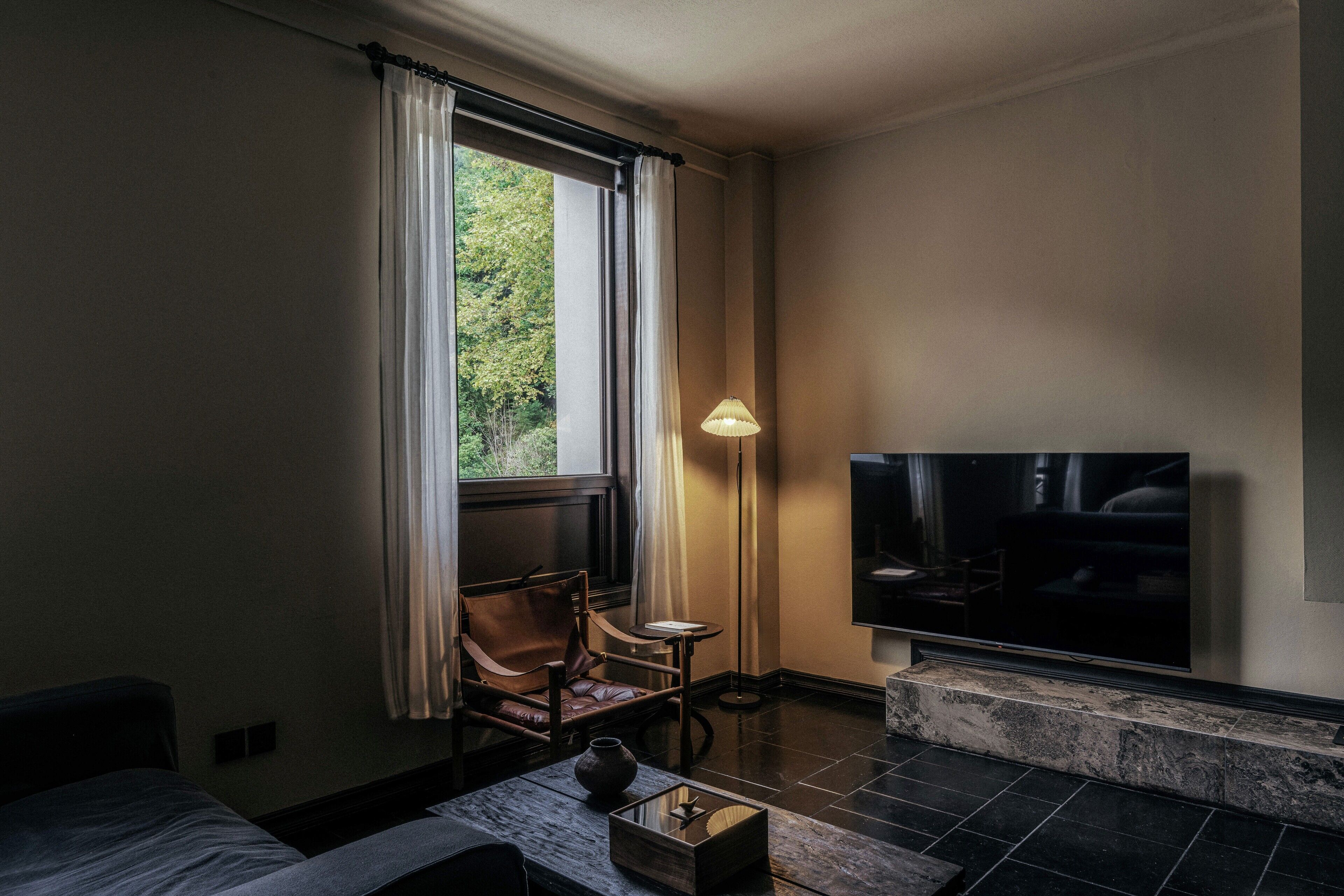 Une chambre d’hôtel comprenant un lit, un coin salon avec une chaise et une table, un téléviseur fixé au mur et une fenêtre avec des rideaux.