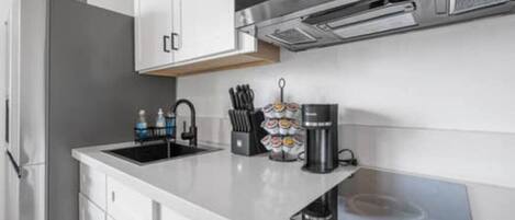 A modern kitchen with a stainless steel range hood, a black coffee maker, and a knife block on the countertop.