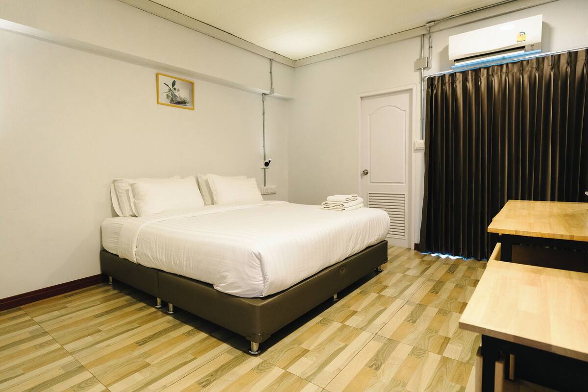 A hotel room with a bed, a table, a door, and a window with curtains.