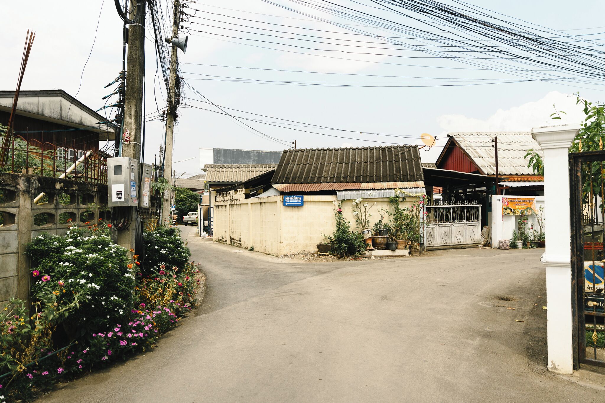 Une rue étroite, bordée de bâtiments des deux côtés, dont certains arborent des enseignes et sont ornés de plantes.