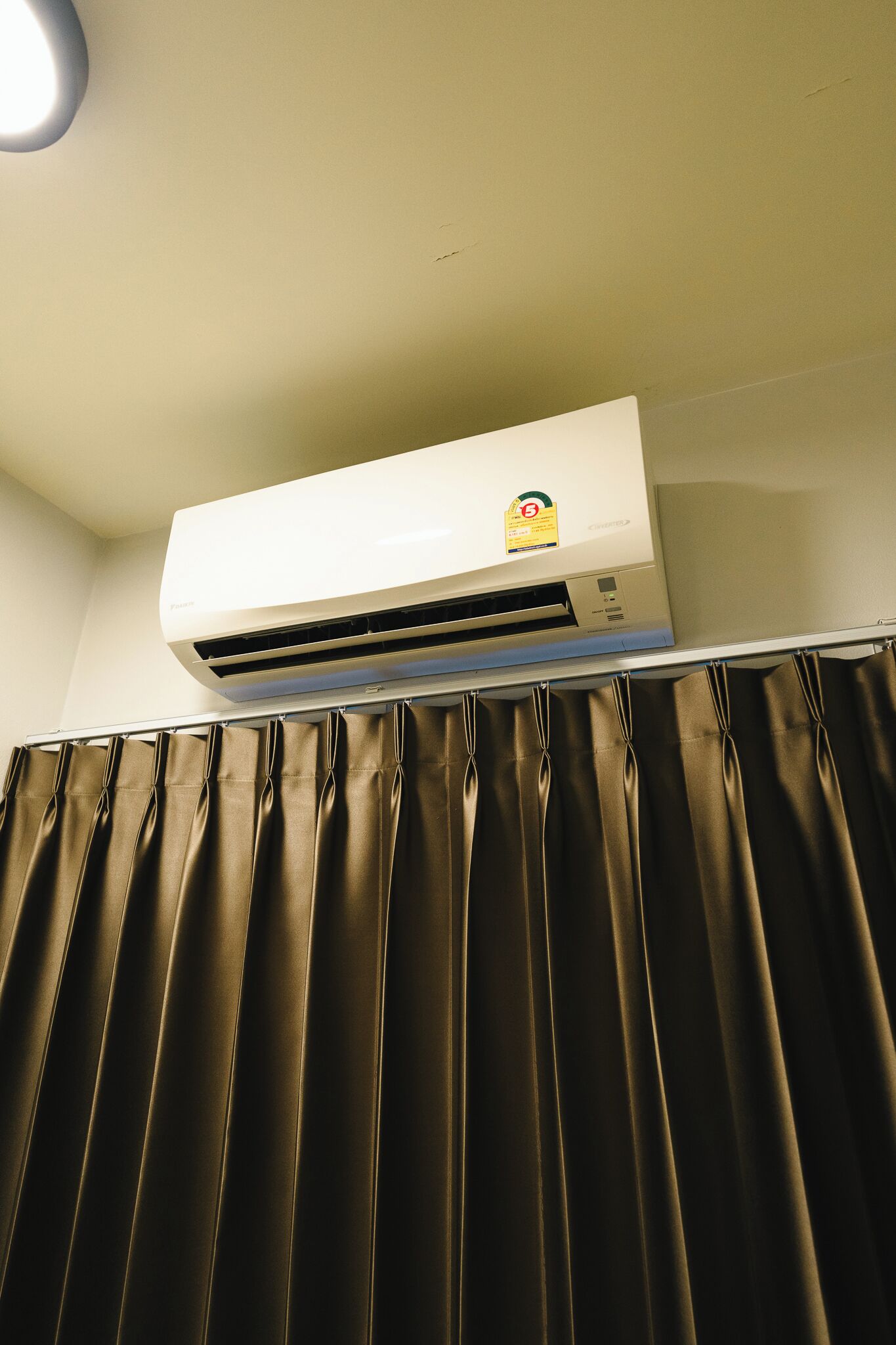 An air conditioning unit mounted on a wall above a curtain.