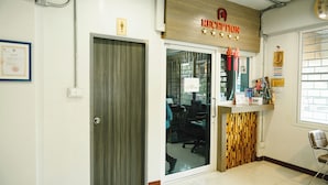 Un área de recepción con un mostrador de madera, una puerta de cristal que da a una oficina y una silla a la derecha.