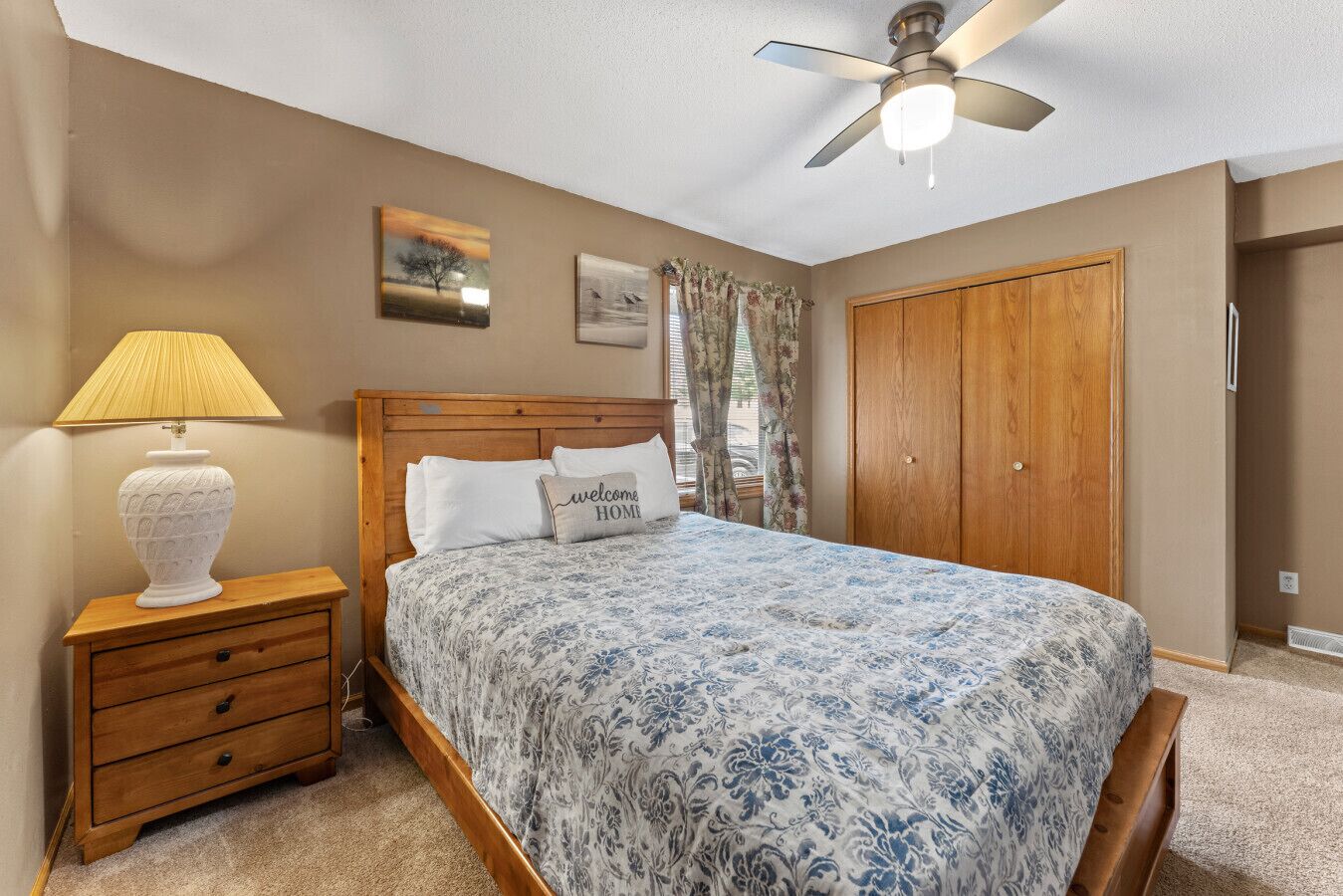 Une chambre à coucher comprenant un lit, une table de chevet, une lampe, un ventilateur de plafond et une armoire.