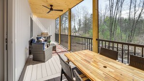Una terraza techada al aire libre con mesa de madera y sillas de mimbre, con vistas a una zona boscosa.