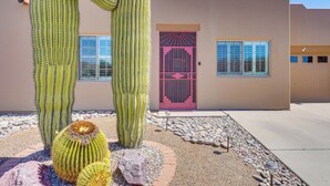 A building with a distinctive pink gate and windows, surrounded by large cacti and a gravel pathway. - Hot Tub Access & Fire Pit: Green Valley Getaway! (Green Valley)