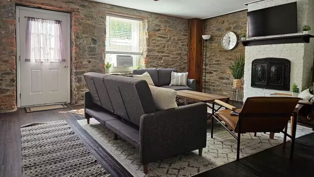 Ein Wohnzimmer mit Steinwand, einer Couch, einem Couchtisch, einem an der Wand montierten Fernseher und einem Deckenventilator.