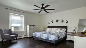 Ein Schlafzimmer mit Bett, Stuhl, Kommode, Nachttisch, Deckenventilator und Wanddekorationen.