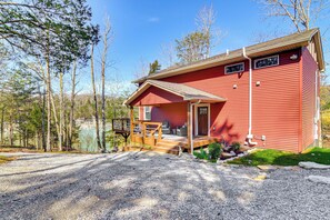 A red cabin with a porch, surrounded by trees and a gravel driveway. - Cumberland Lake Retreat: Furnished Deck & Grill! (Burnside)