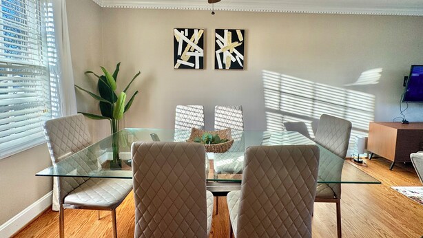 A dining area with a glass table, cushioned chairs, a ceiling fan, and artwork on the wall. - 4BR Home BoA, Discovery, Raptor, USNWC & Uptown (Charlotte)