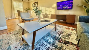A living room with a flat-screen TV, a ceiling fan, a dining table, and a patterned rug. - 4BR Home BoA, Discovery, Raptor, USNWC & Uptown (Charlotte)