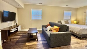 A modern living room with a sofa, a coffee table, a TV, and a bed. - 4BR Home BoA, Discovery, Raptor, USNWC & Uptown (Charlotte)