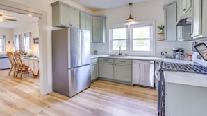 Una cocina moderna con armarios verde claro, electrodomésticos de acero inoxidable y suelo de madera.