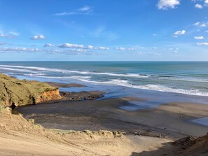 Un paysage côtier avec une plage, des falaises rocheuses et un ciel dégagé.
