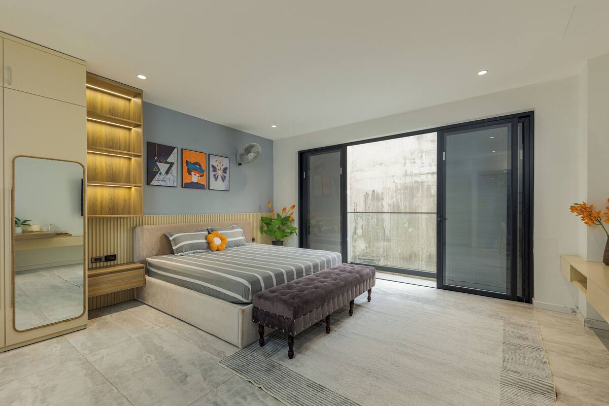 A modern bedroom with a large bed, a bench, a sliding glass door, and a mirror.