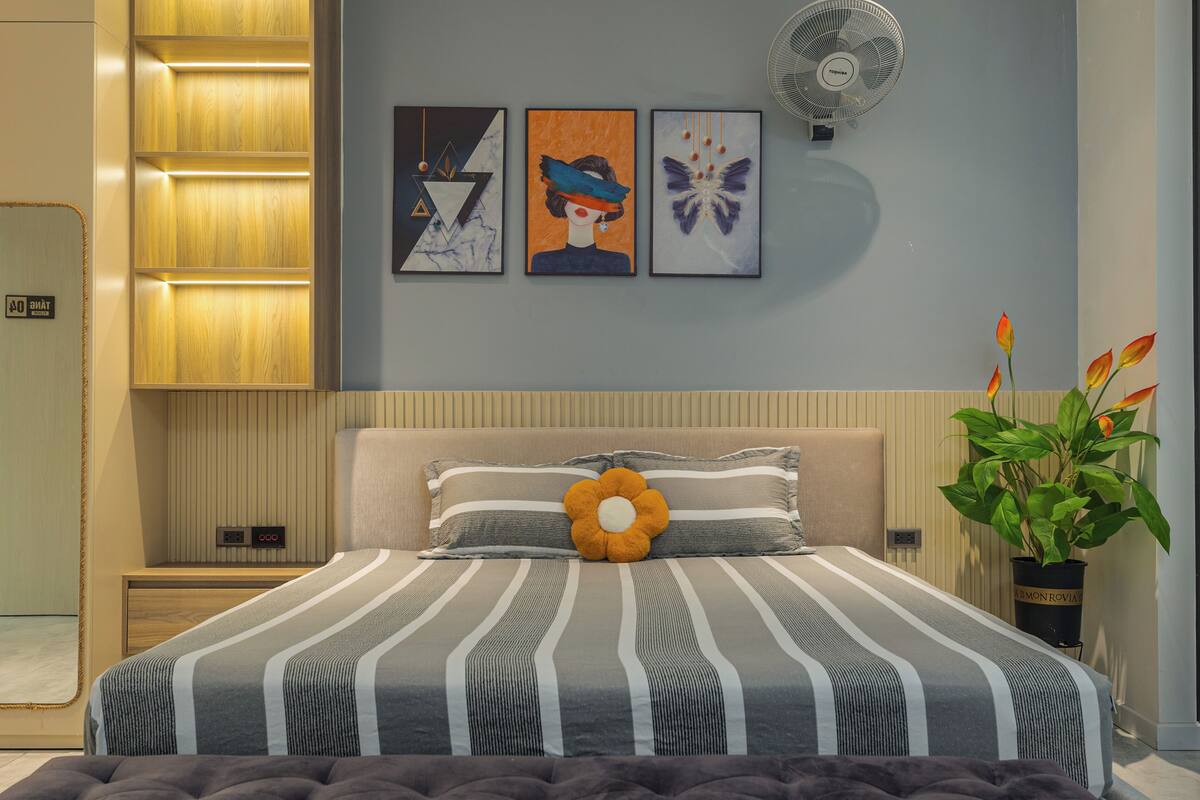A modern bedroom with a bed, a nightstand, a wall-mounted fan, and three framed artworks.
