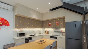 A modern kitchen with a wooden dining table, grey chairs, a microwave, a sink, and a refrigerator. - Thao Nguyen Homestay Ha Noi (Hanoi)