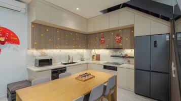 Cocina moderna con mesa de madera, sillas grises, microondas, lavaplatos y refrigerador.
