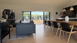 A modern living room with a sofa, a coffee table, and a dining area with chairs and a table. - Goolwa Beach Pavilion (Goolwa Beach)