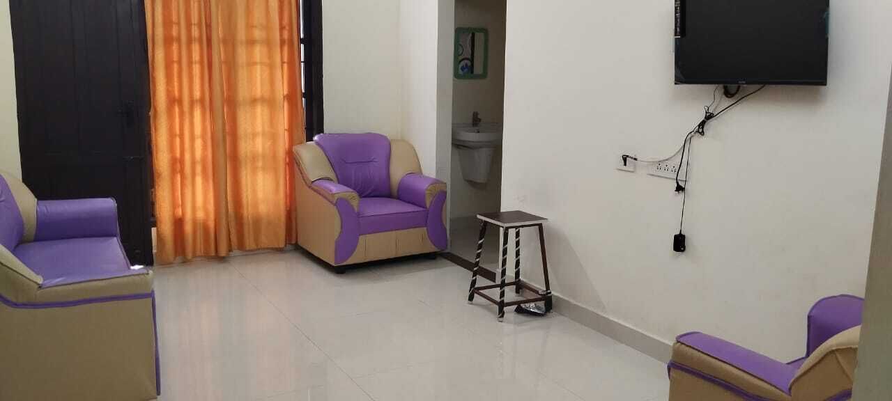 Una sala de estar con sillones morados y beige, una mesita y un televisor montado en la pared.