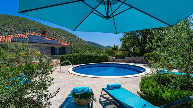 A swimming pool with lounge chairs and an umbrella, surrounded by greenery and a house with a tiled roof. - Villa Kate - Dubrovnik by Villas Guide (Dubrovnik)