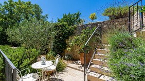 A patio with a table and chairs, surrounded by lush greenery and a stone wall. - Villa Kate - Dubrovnik by Villas Guide (Dubrovnik)