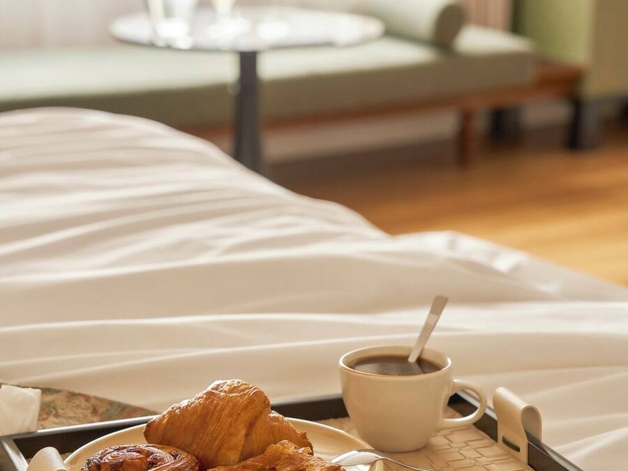 A breakfast tray with pastries and coffee on a bed in a hotel room.