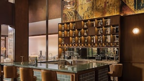 Una zona de bar con una barra alargada, varios taburetes y estantes llenos de botellas y vasos.