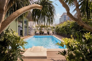 A swimming pool with lounge chairs, surrounded by greenery and palm trees, with a modern building in the background. - M Village Hotel Premier Thi Sách, a brand of Modern Village Lifestyle (Ho Chi Minh City)