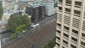 A high-rise building with multiple floors, a railway track with a train, and a cityscape with various buildings.