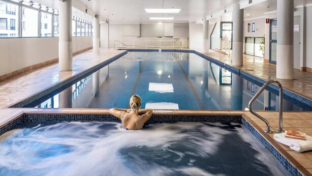A large indoor swimming pool with clear lanes, a central water feature, and a view of the outside through large windows.