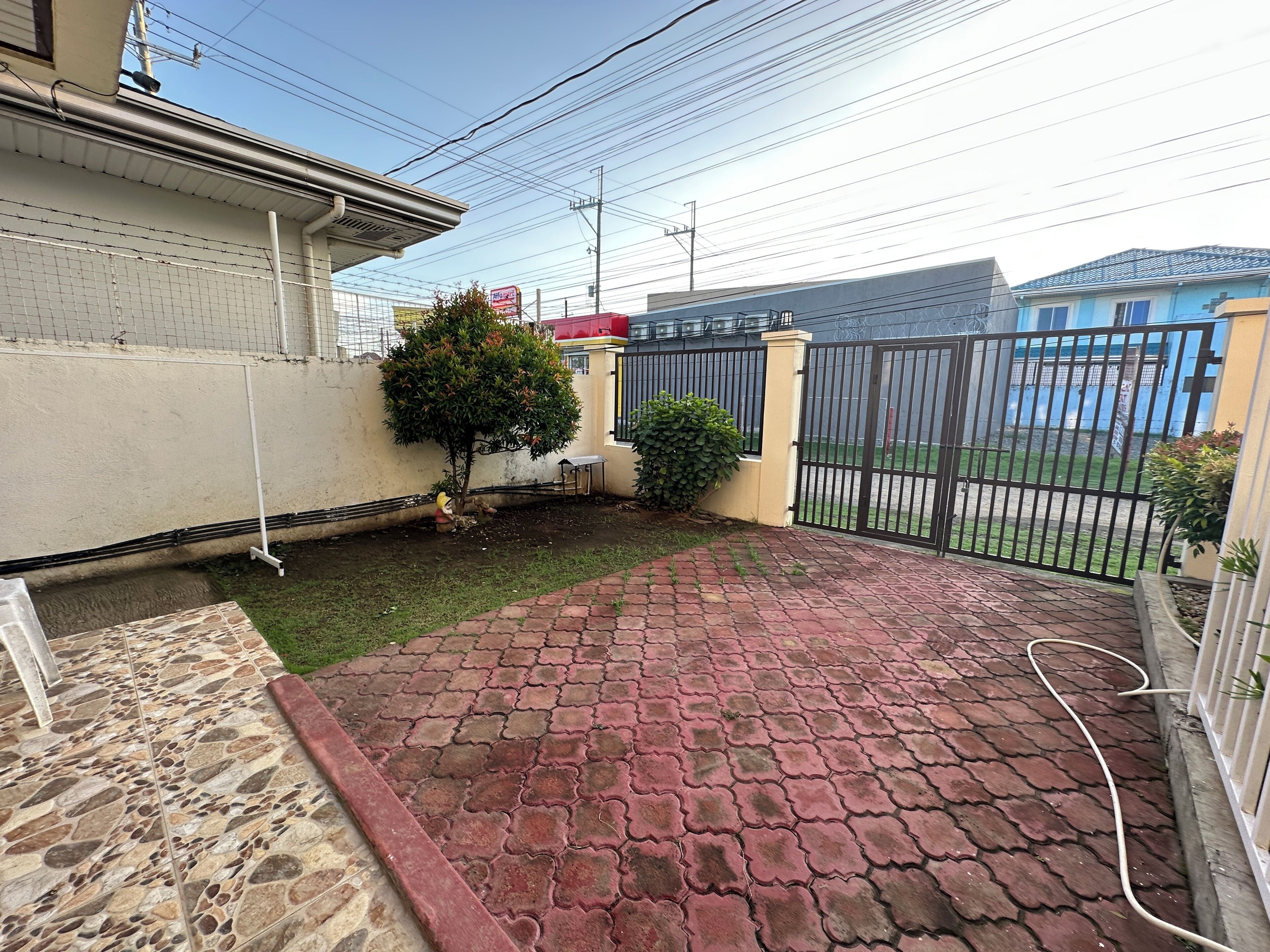 Une terrasse dallée avec un motif en briques, une petite pelouse et une clôture en métal.