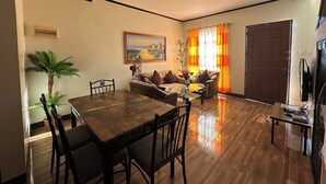 Una sala de estar con una mesa de comedor, sillas, un sofá, un televisor y una puerta.
