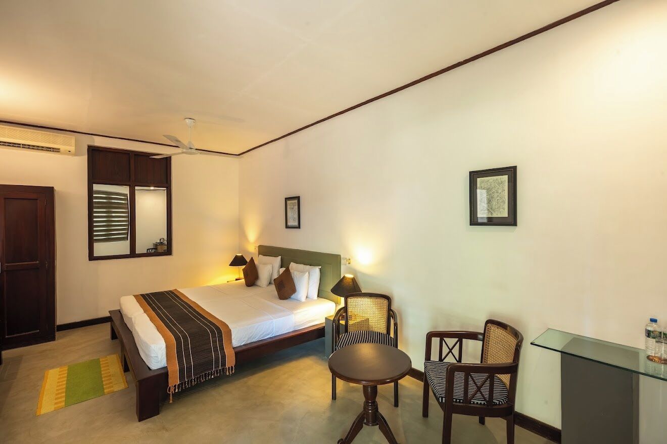 A hotel room with a bed, bedside table, two chairs, a desk, and a mirror.