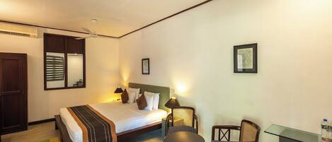 A hotel room with a bed, bedside table, two chairs, a desk, and a mirror.