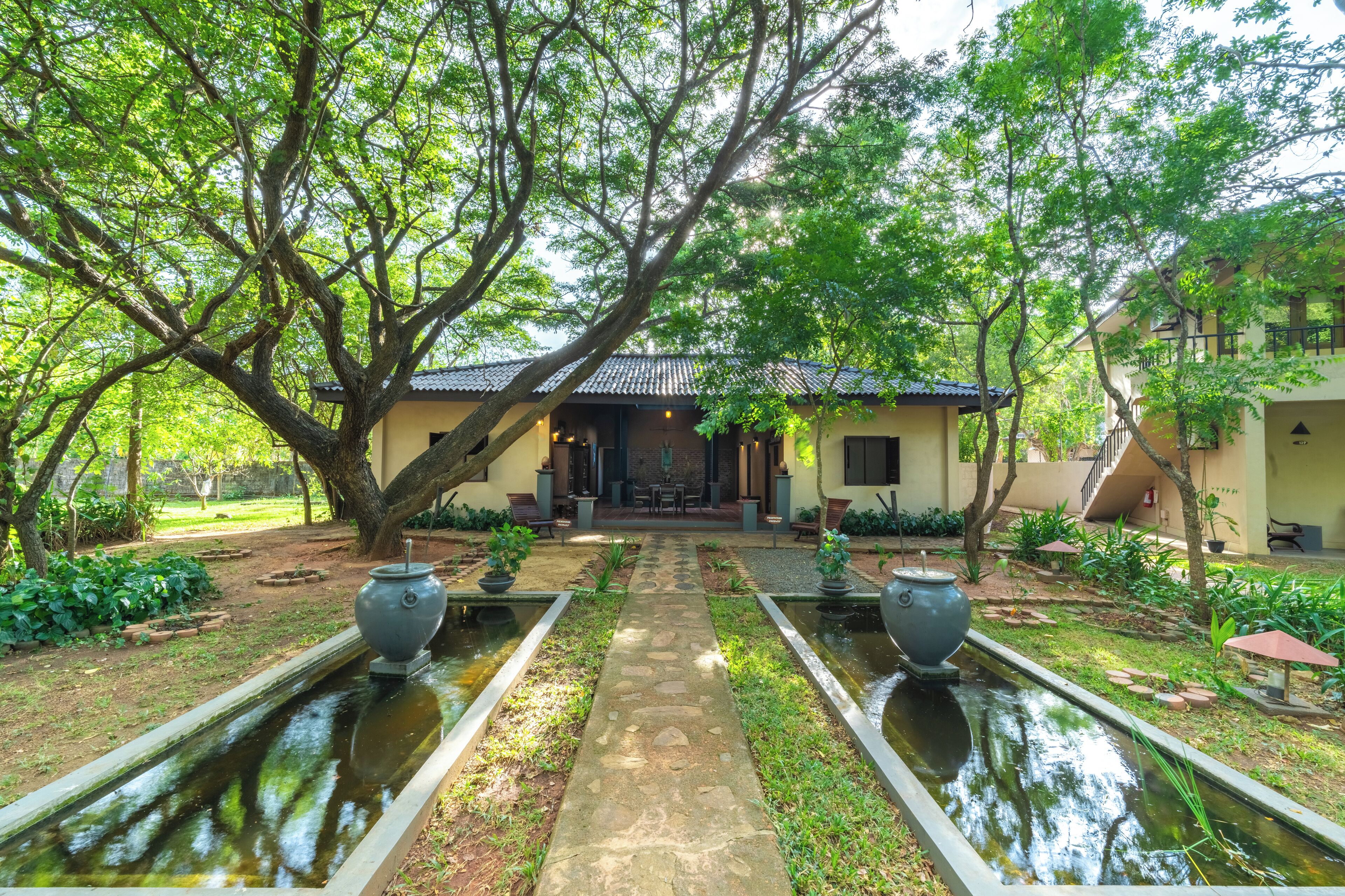 A traditional building with a tiled roof, surrounded by lush greenery and a central pathway leading to a seating area.