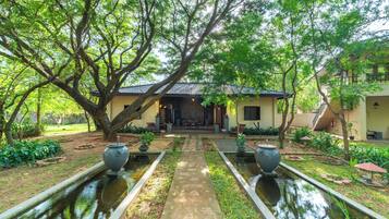 A traditional building with a tiled roof, surrounded by lush greenery and a central pathway leading to a seating area.