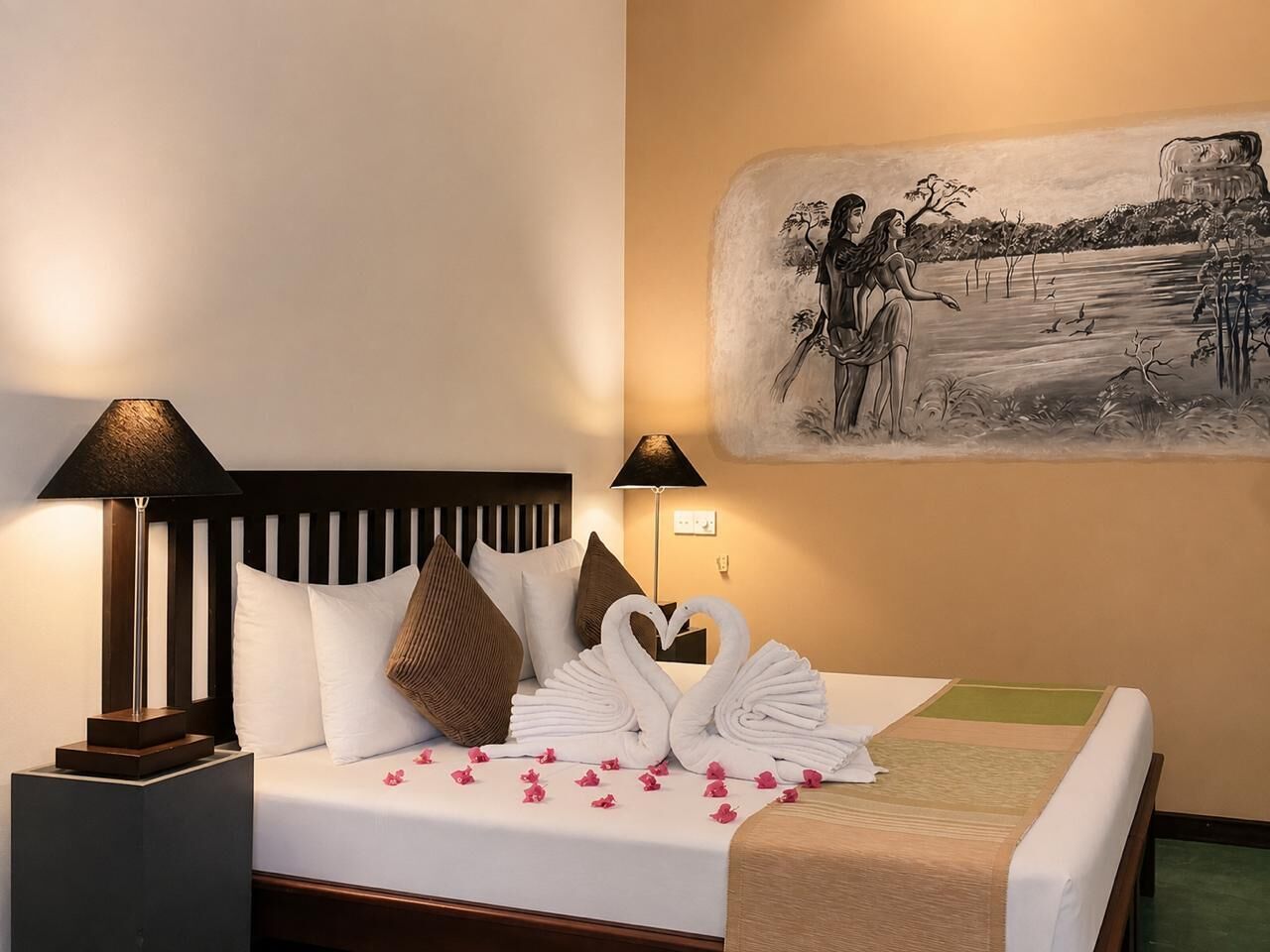 A hotel room with a bed, pillows, a wall-mounted painting, and a nightstand with a lamp.
