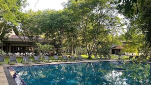 A swimming pool surrounded by lounge chairs and trees, with a building in the background. - Kassapa Lion Rock  (Sigiriya)