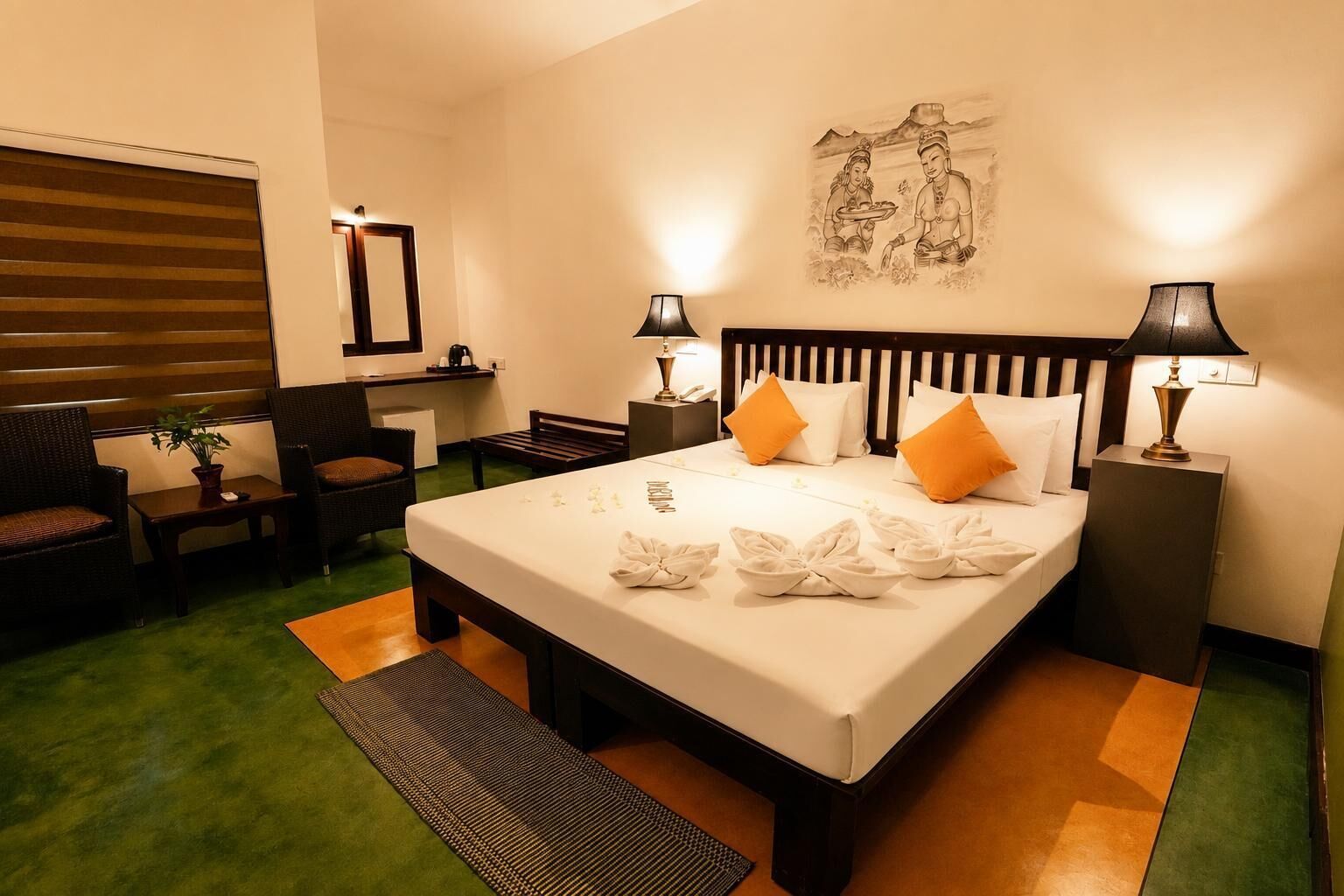 Quarto de hotel com uma cama grande, duas luminárias de cabeceira, uma escrivaninha com cadeira, um espelho e uma obra de arte pendurada na parede.