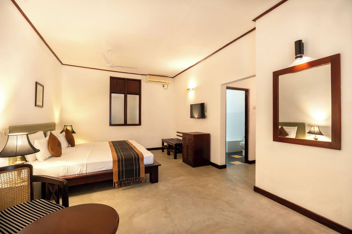 A hotel room with a bed, bedside table, lamp, chair, and a large mirror.