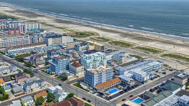An aerial view of a coastal town with a beachfront, multi-story buildings, and a parking lot.