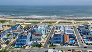 A coastal hotel with multiple buildings, a parking lot, and a beach view.