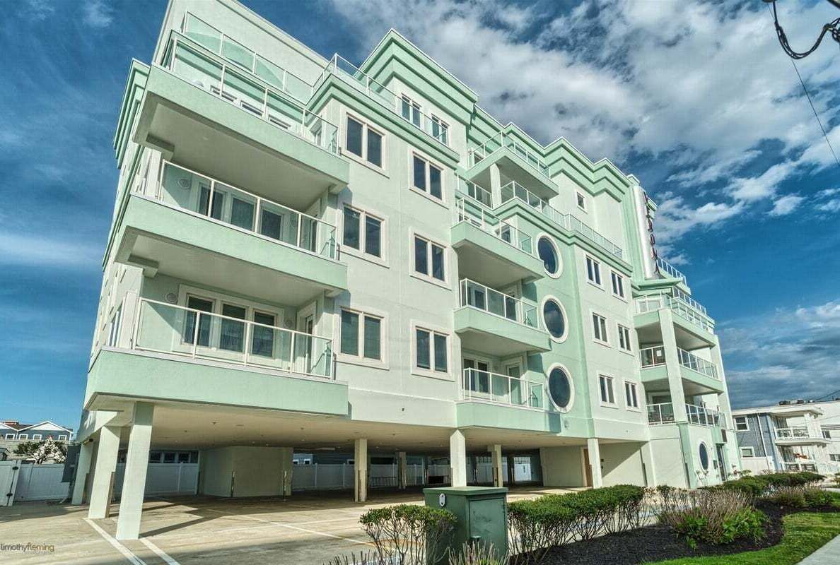 A multi-story building with balconies, a flat roof, and a parking area.