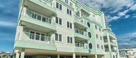 A multi-story building with balconies, a flat roof, and a parking area.