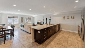 A modern kitchen with a large island, dark cabinetry, and a dining area with a table and chairs.