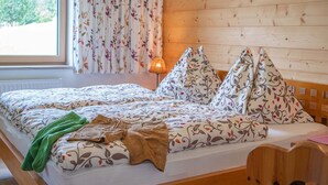 En säng med blommigt sänglinne, en lampa och utsikt över träd genom ett fönster.