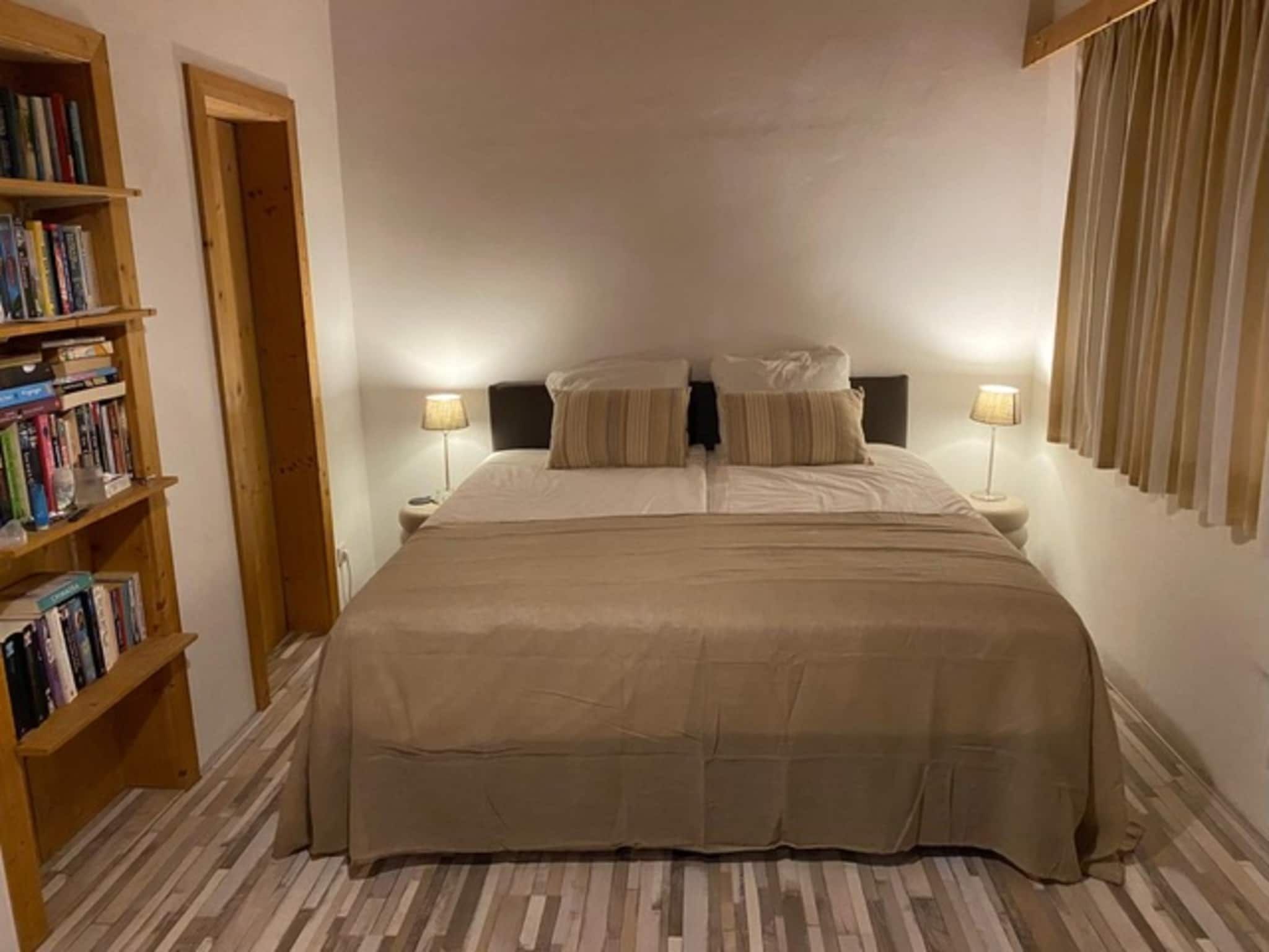 Une chambre à coucher avec un grand lit, deux tables de chevet avec des lampes, une bibliothèque en bois et une porte.