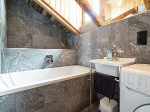A bathroom with a bathtub, a sink, and a washing machine. - Vacation in Kaprun: A chalet surrounded by nature (Kaprun)