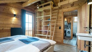 A wooden cabin interior with a bed, a ladder to a loft, a washing machine, and a sink.